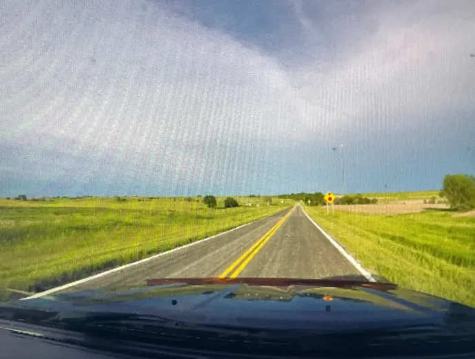 A screenshot of AmericaOS: What appears to be a view from the inside of a car’s driver seat, looking out at a field of grass.