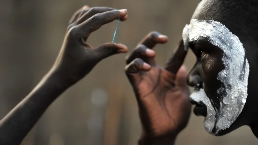 A photograph of a person using a shard of a mirror to paint their own face