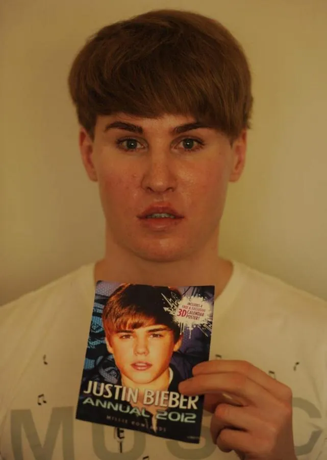 A photograph of a Justin Beiber lookalike. The lookalike is holding an event flyer for a Justin Beiber concert